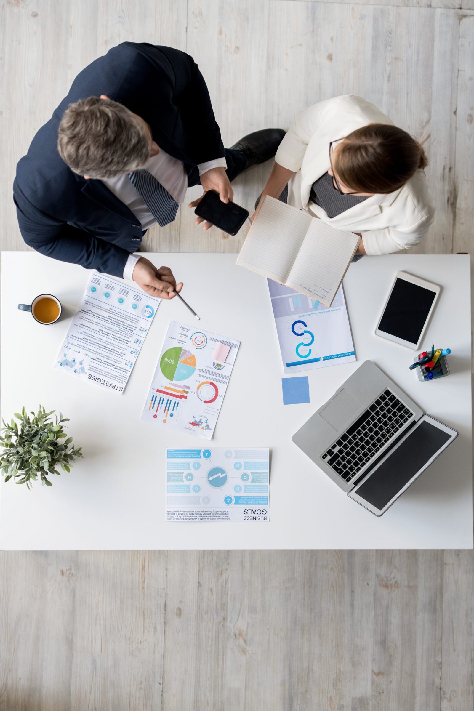 Directly above view of confident business colleagues standing at table in office and discussing plans while allocating tasks among each other